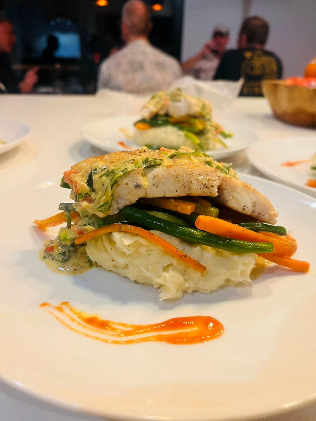 Plato de pescado sobre puré servido en la mesa con el grupo cenando al fondo